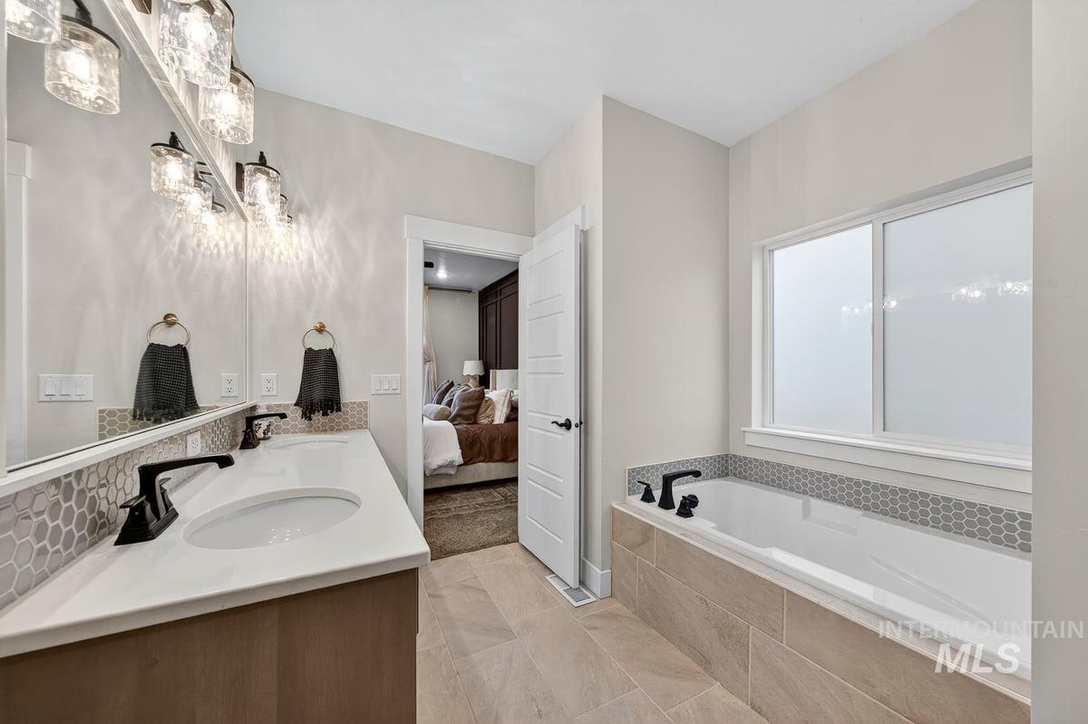 Ensuite bathroom featuring double vanity, a bath, and light tile patterned flooring