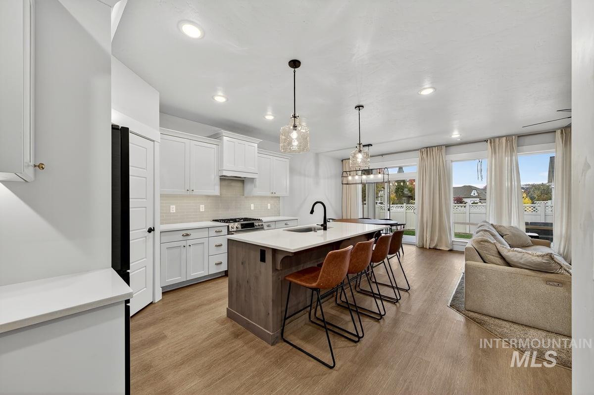 Kitchen with white cabinets, a kitchen breakfast bar, tasteful backsplash, an island with sink, and decorative light fixtures