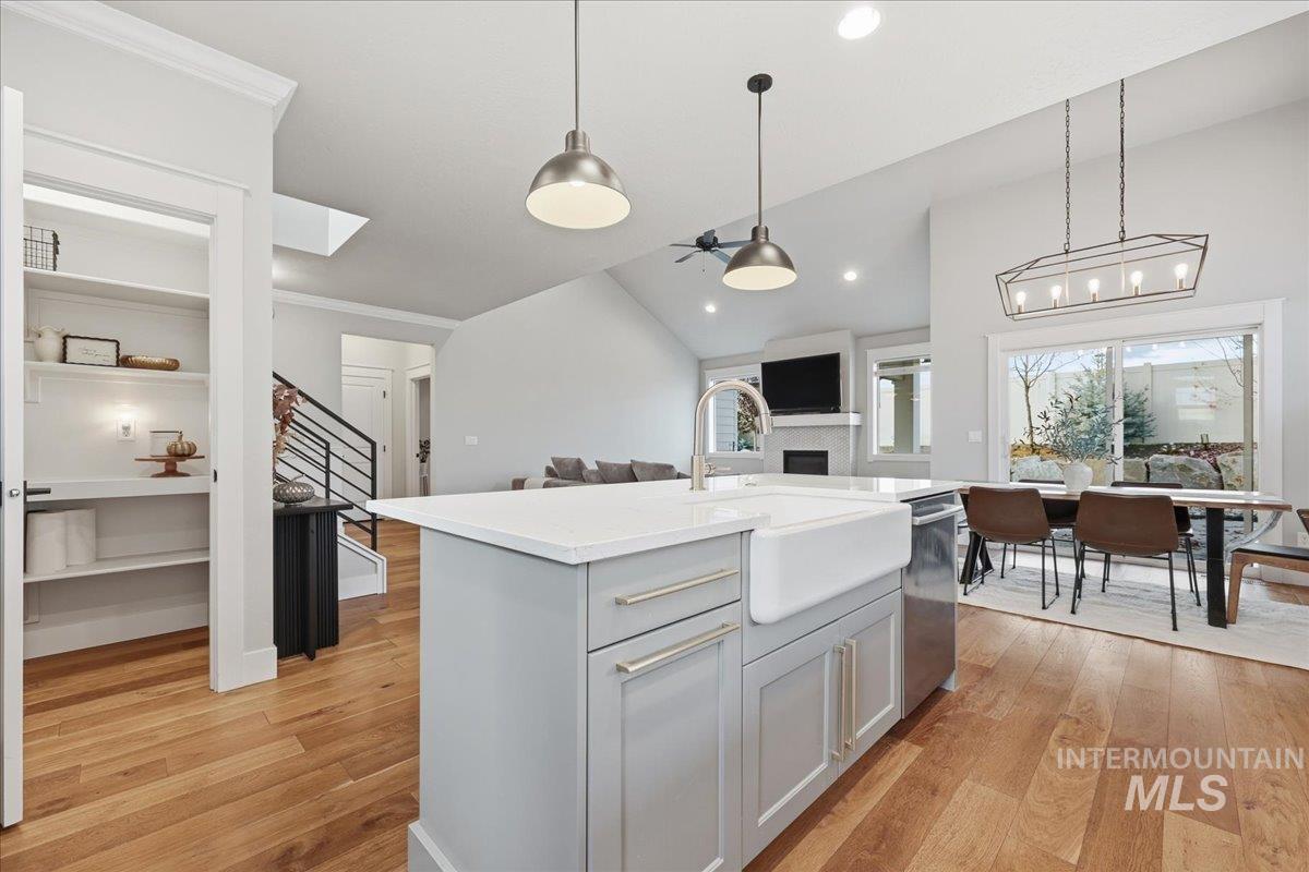 Kitchen with light wood-style flooring, pendant lighting, open floor plan, lofted ceiling, and a center island with sink