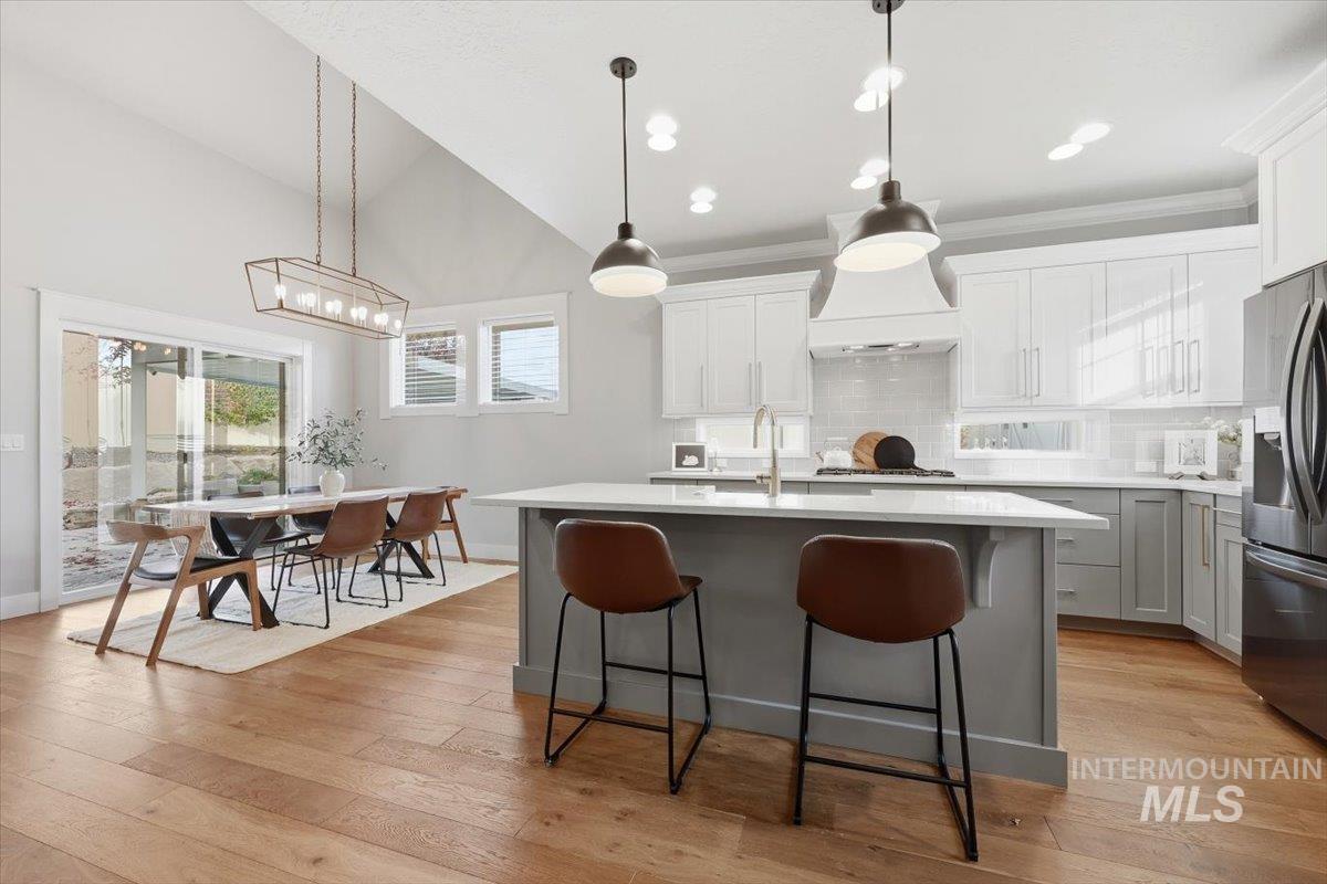Kitchen featuring backsplash, gray cabinetry, pendant lighting, stainless steel fridge, and vaulted ceiling