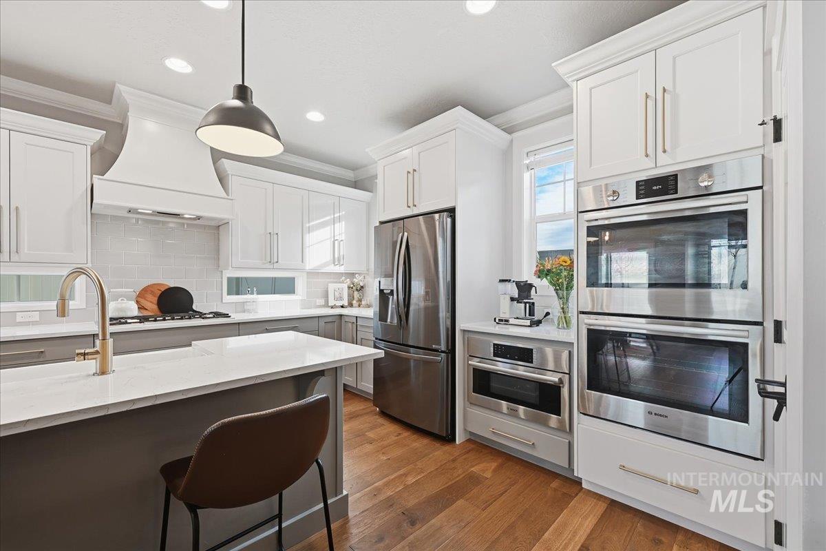 Kitchen featuring appliances with stainless steel finishes, tasteful backsplash, dark wood-type flooring, light stone counters, and white cabinets