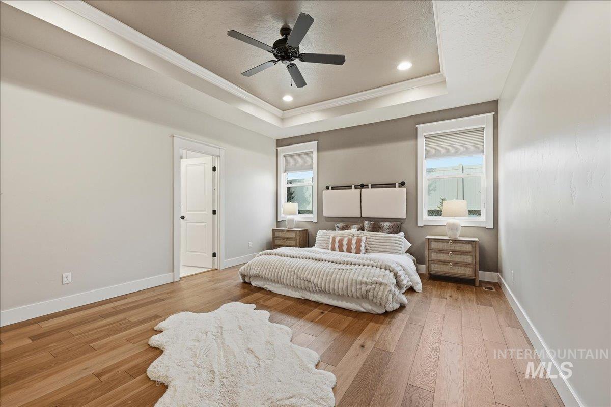 Bedroom with a tray ceiling, ornamental molding, light wood-style flooring, a textured ceiling, and recessed lighting