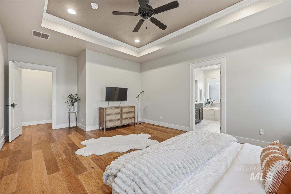 Bedroom featuring a raised ceiling, ornamental molding, wood finished floors, recessed lighting, and ceiling fan