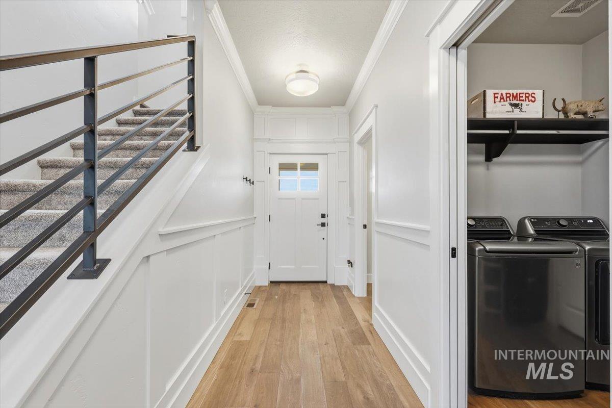 Laundry room with ornamental molding, washer and dryer, light wood-style floors, and a decorative wall