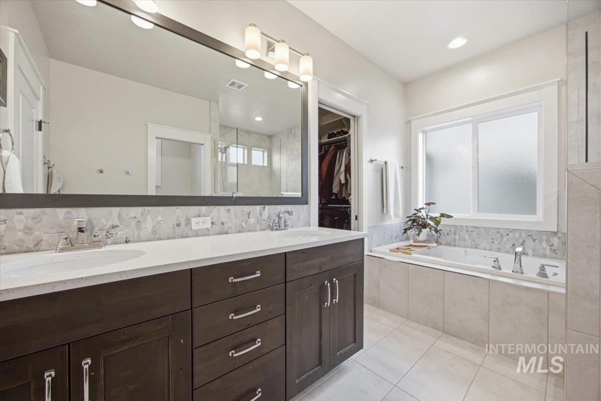 Bathroom with double vanity, light tile patterned floors, a garden tub, and a walk in closet