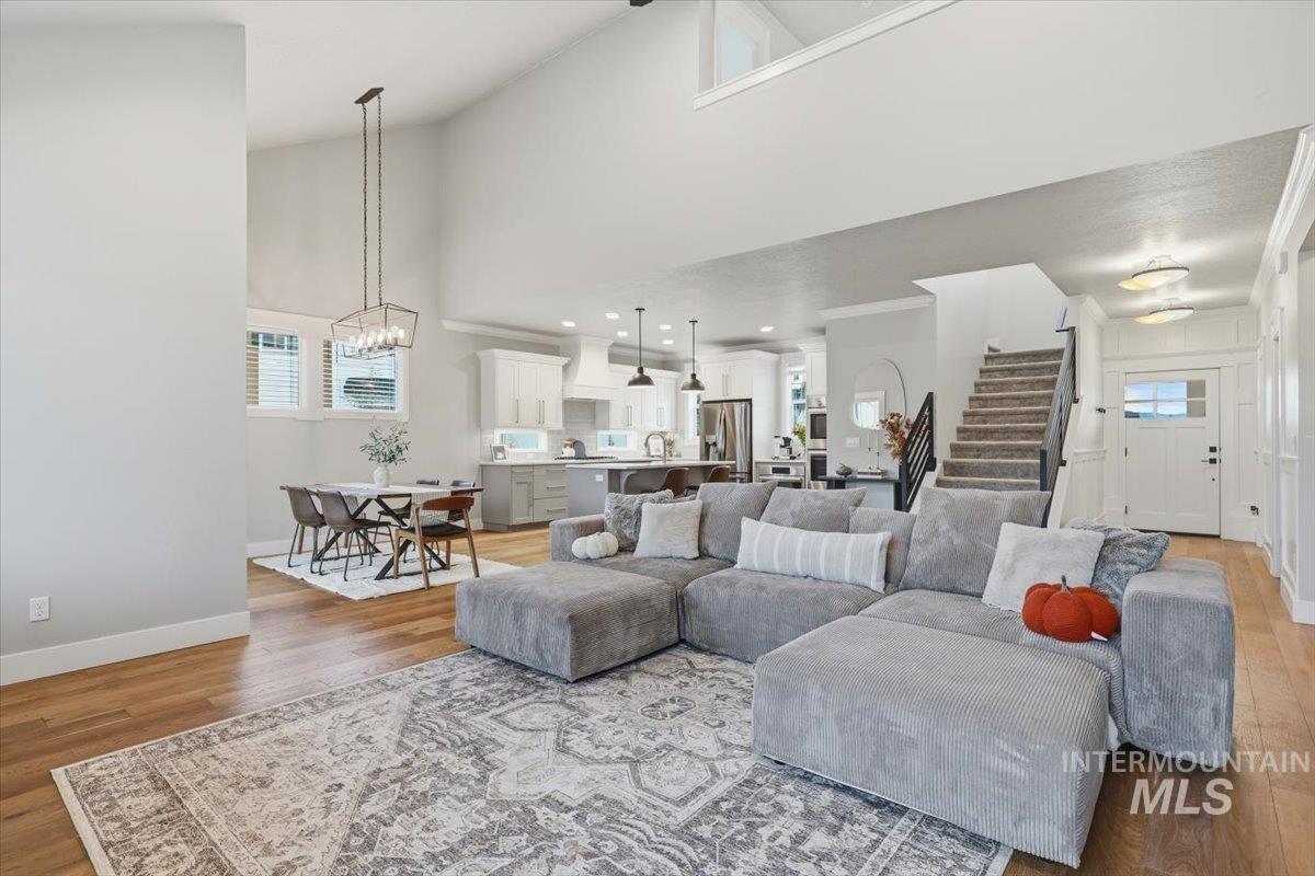 Living room with high vaulted ceiling, stairway, light wood-style flooring, and a chandelier