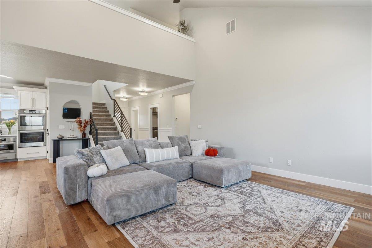 Living area featuring high vaulted ceiling, light wood-type flooring, stairway, and ornamental molding