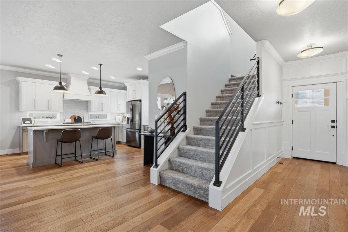 Entryway with stairs, crown molding, light wood-style flooring, a textured ceiling, and a decorative wall