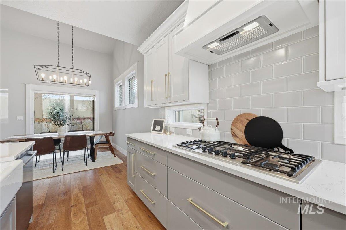 Kitchen with premium range hood, light wood finished floors, decorative light fixtures, tasteful backsplash, and gray cabinetry