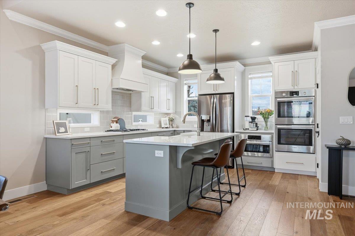 Kitchen with gray cabinets, appliances with stainless steel finishes, a kitchen bar, pendant lighting, and a kitchen island with sink