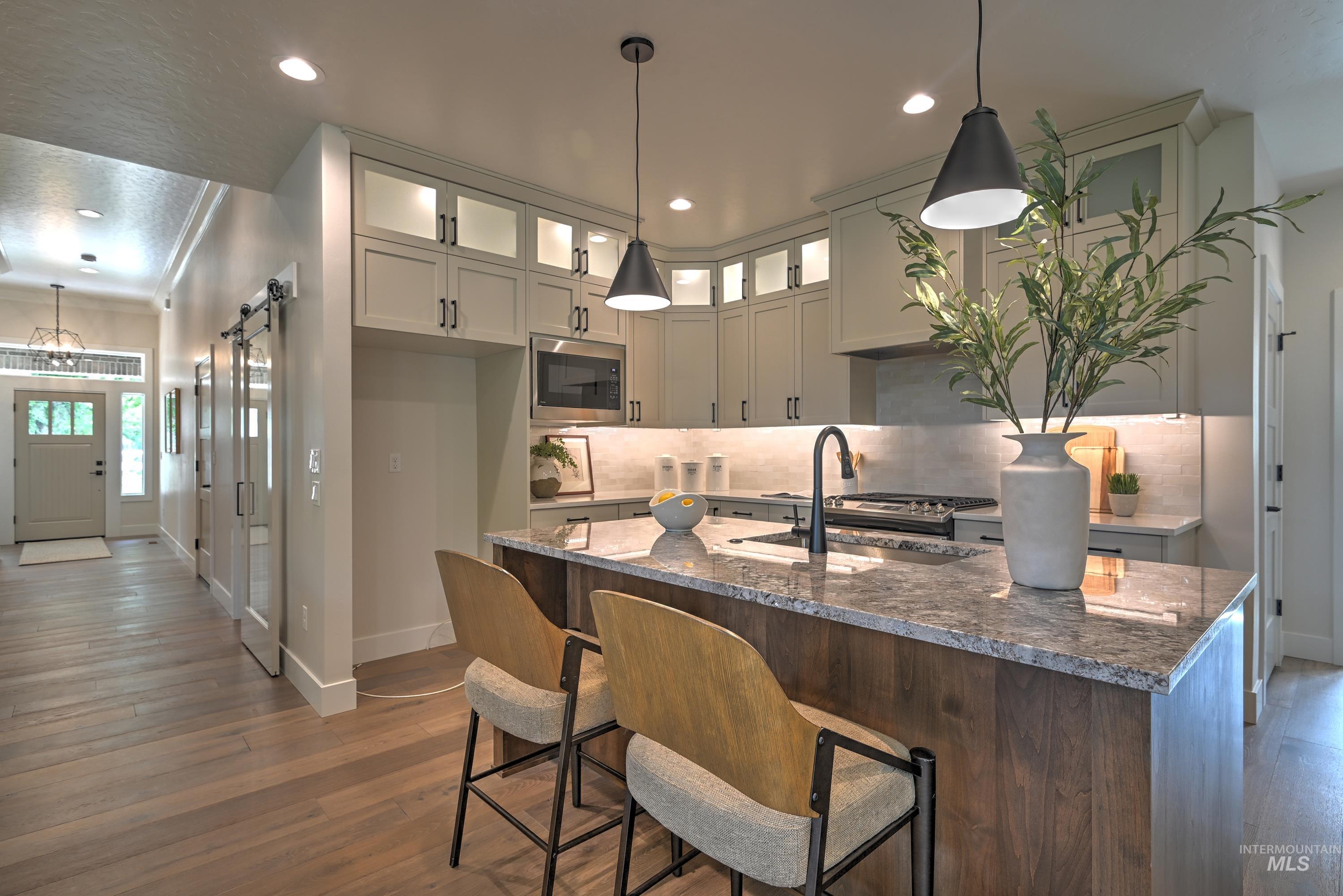 Kitchen featuring glass insert cabinets, quartz & granite  counters, a kitchen island with sink, full tile backsplash, and decorative light fixtures