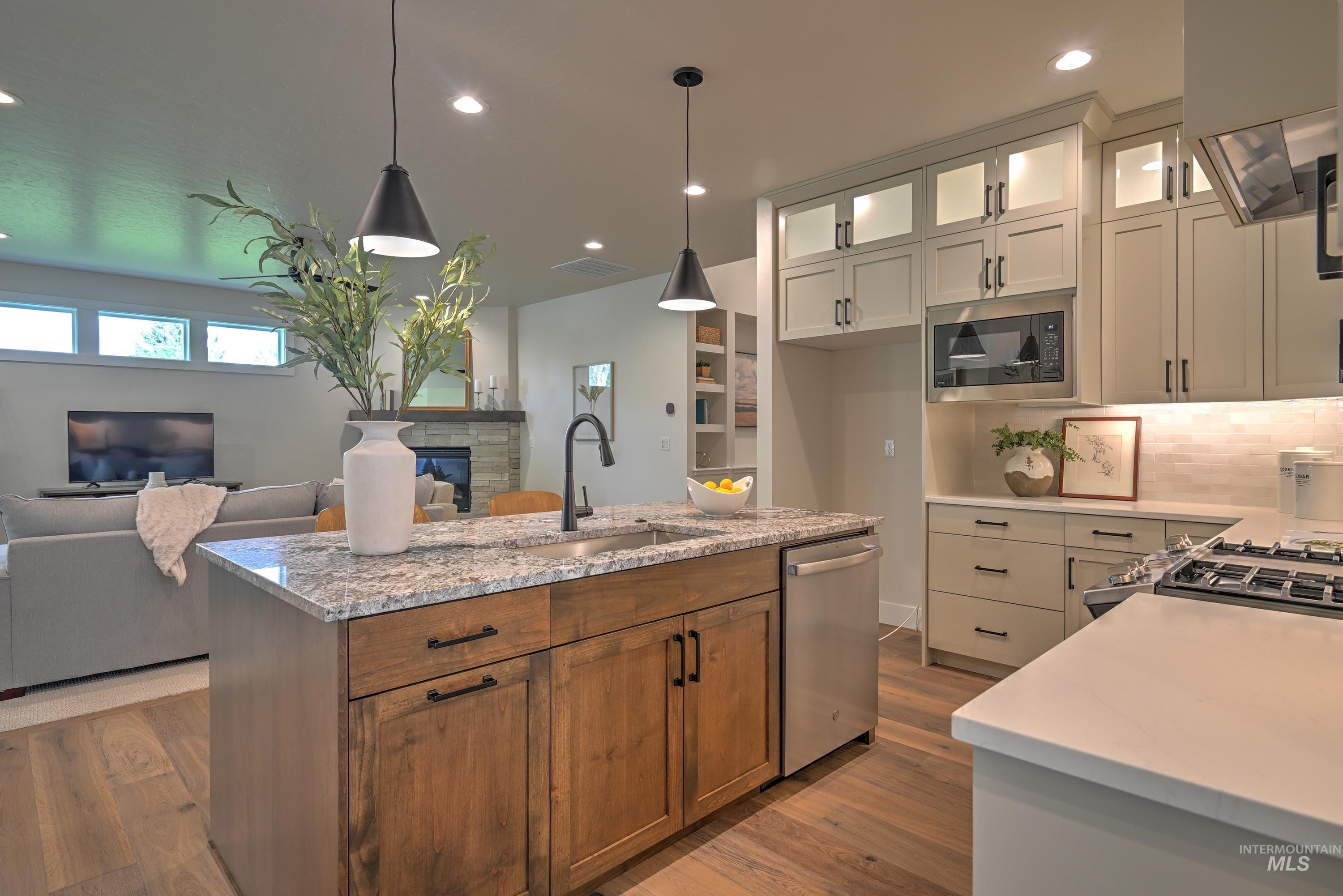 Kitchen with ceiling height custom alder wood cabinetry, light stone counters, light wood finished floors, hanging light fixtures, and recessed lighting