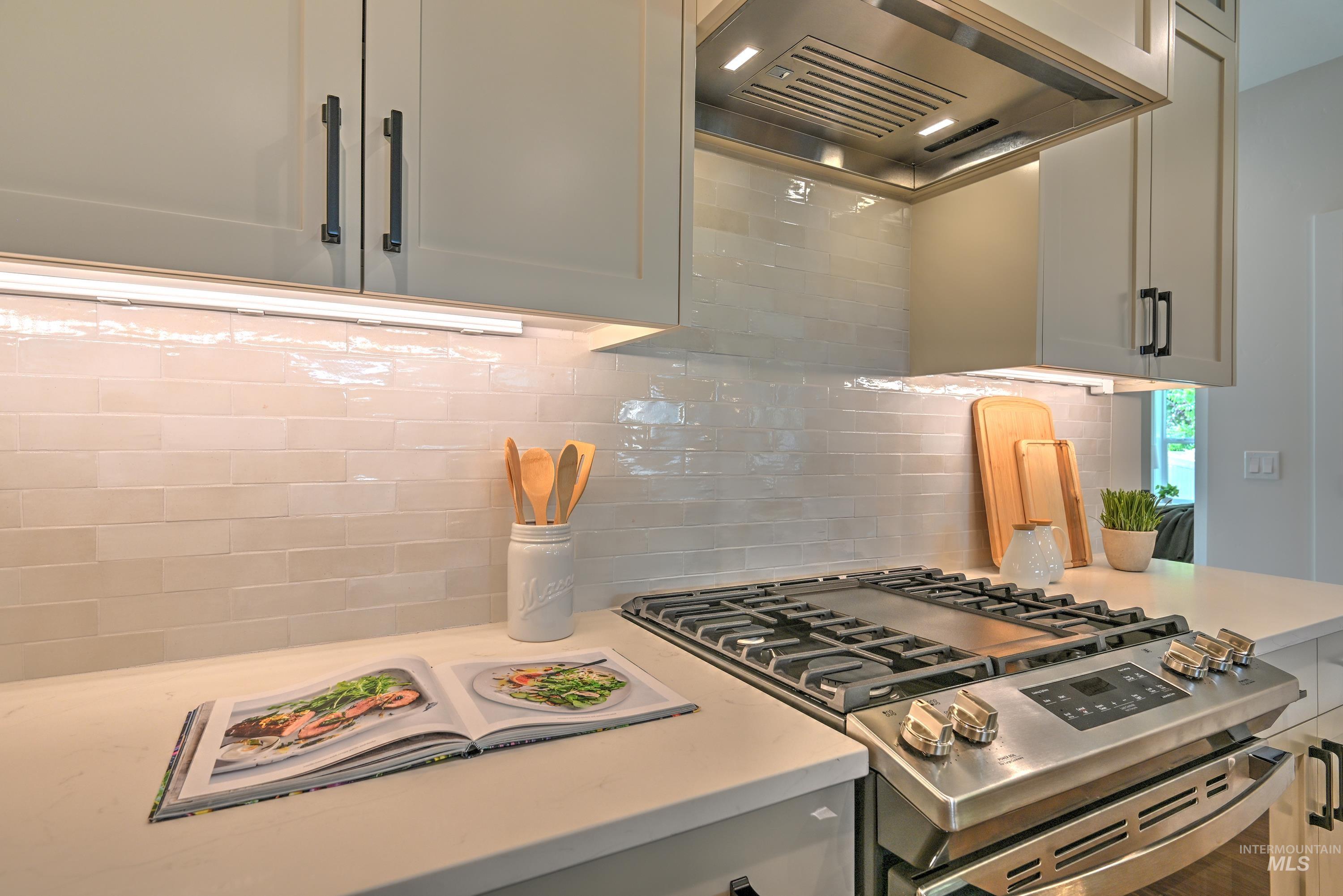 Kitchen with stainless steel range with gas cooktop, wall chimney exhaust hood, full tile backsplash, and quartz & granite counters