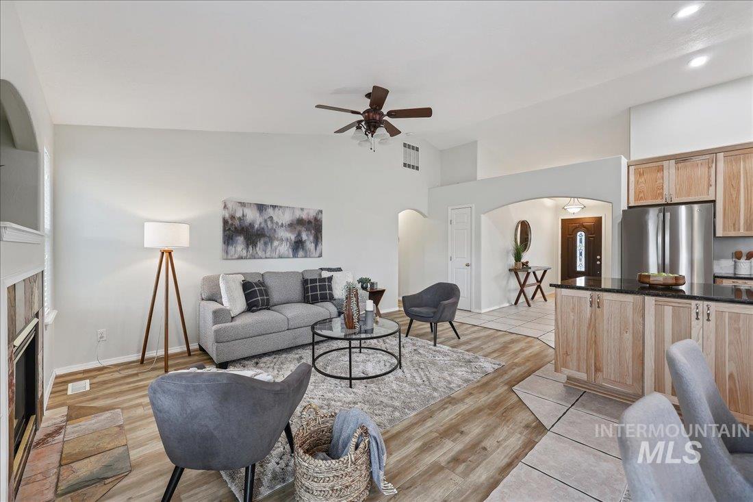 Living room with arched walkways, a tiled fireplace, light wood-type flooring, vaulted ceiling, and ceiling fan