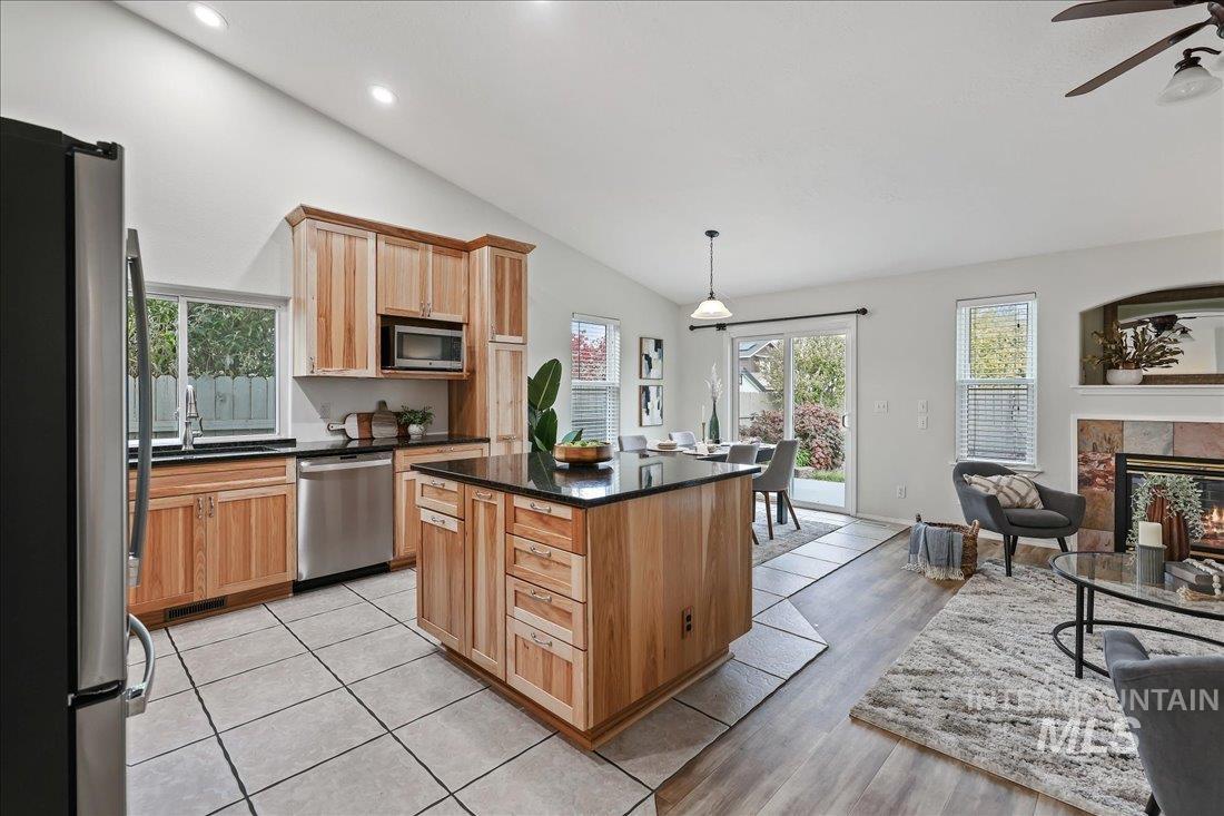 Kitchen with appliances with stainless steel finishes, vaulted ceiling, a tiled fireplace, pendant lighting, and open floor plan