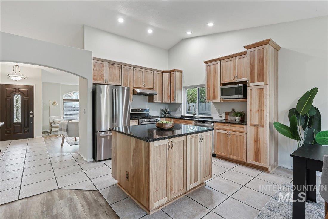 Kitchen featuring arched walkways, stainless steel appliances, light tile patterned floors, dark stone counters, and light brown cabinetry