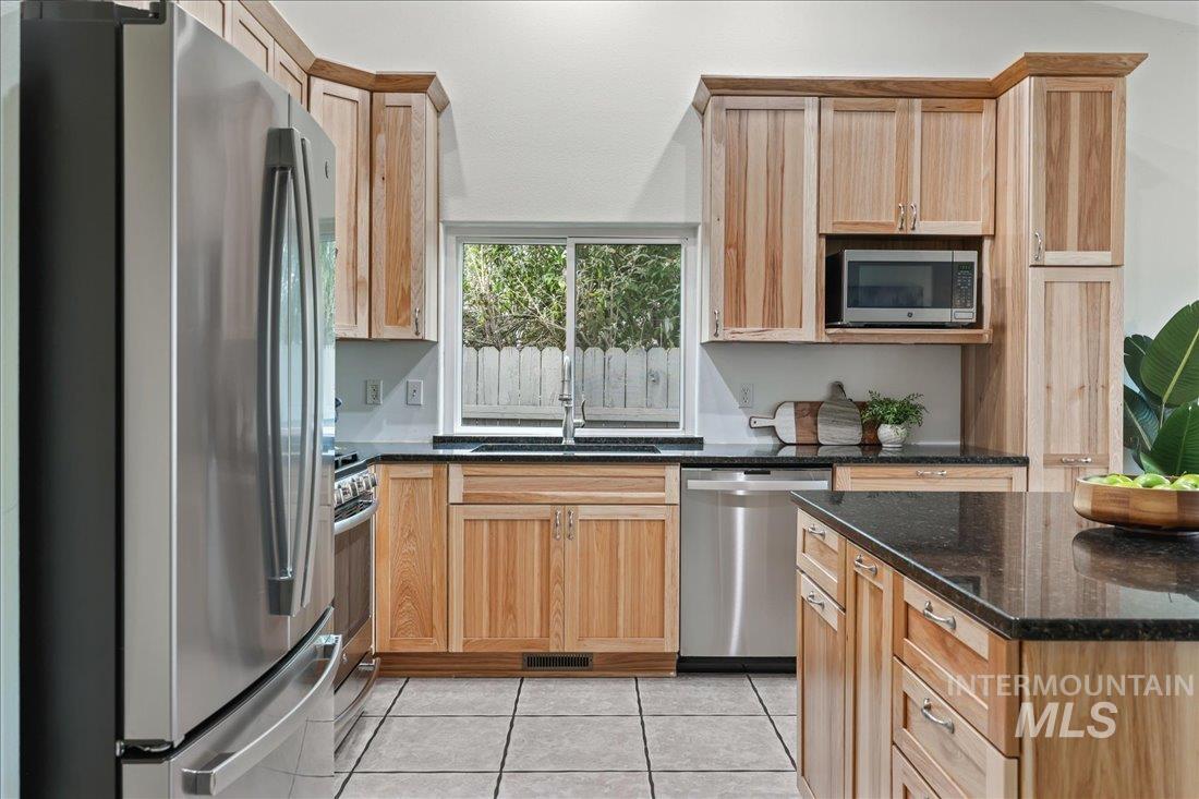 Kitchen with stainless steel appliances, dark stone countertops, light tile patterned floors, and light brown cabinetry