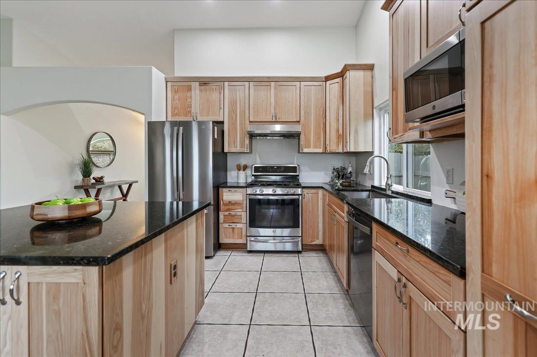 Kitchen with dark stone countertops, appliances with stainless steel finishes, light brown cabinetry, and light tile patterned floors