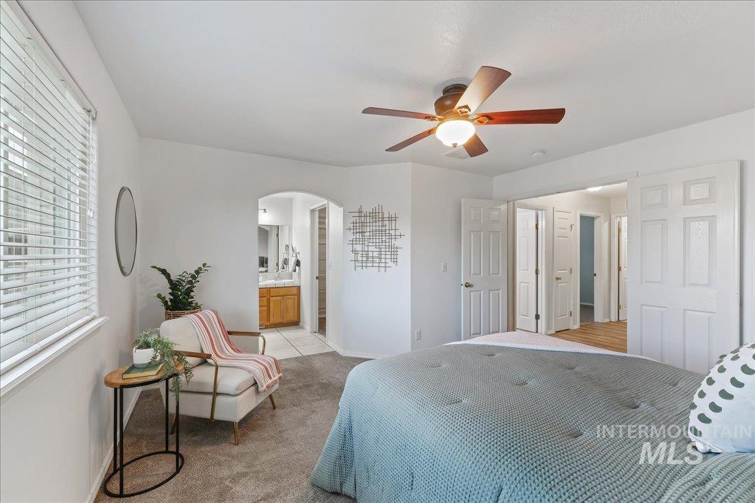 Bedroom with light colored carpet, a ceiling fan, connected bathroom, and arched walkways