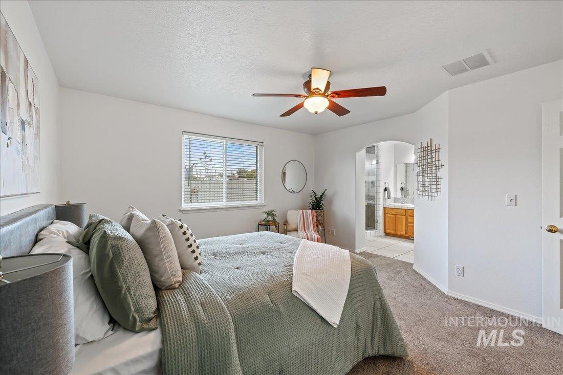 Carpeted bedroom featuring ensuite bathroom, arched walkways, a textured ceiling, and ceiling fan