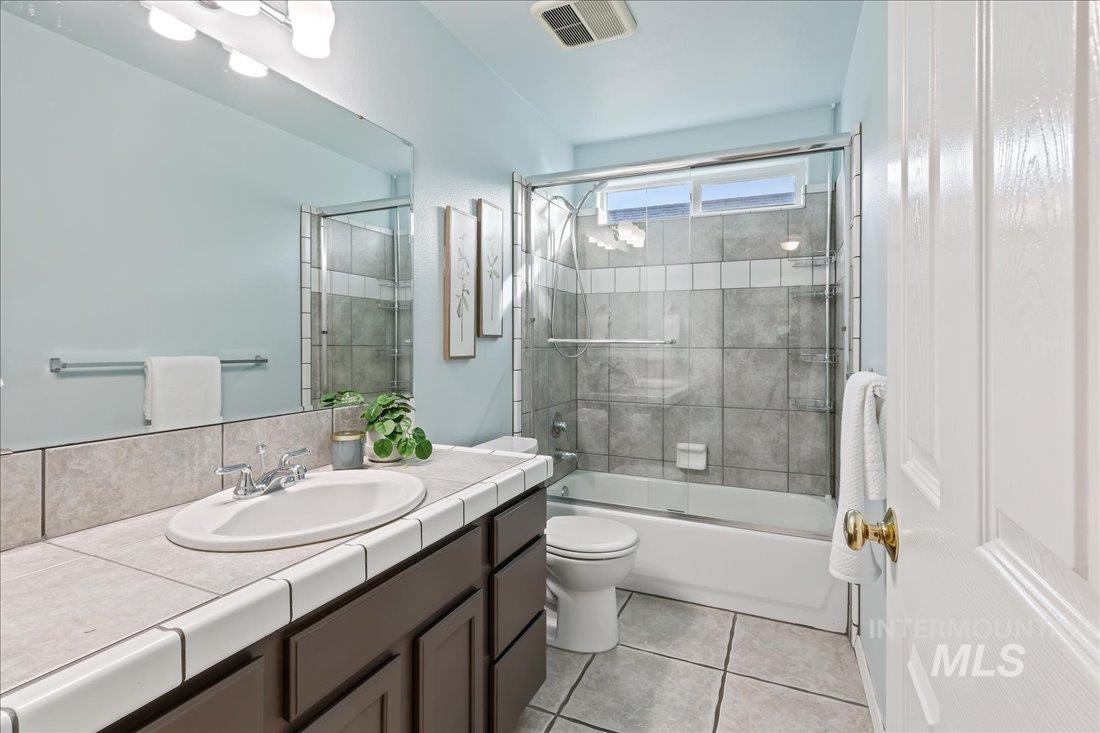 Full bath with combined bath / shower with glass door, vanity, and light tile patterned flooring