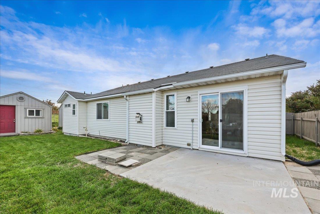 Rear view of house featuring a patio area, a storage unit, and roof with shingles