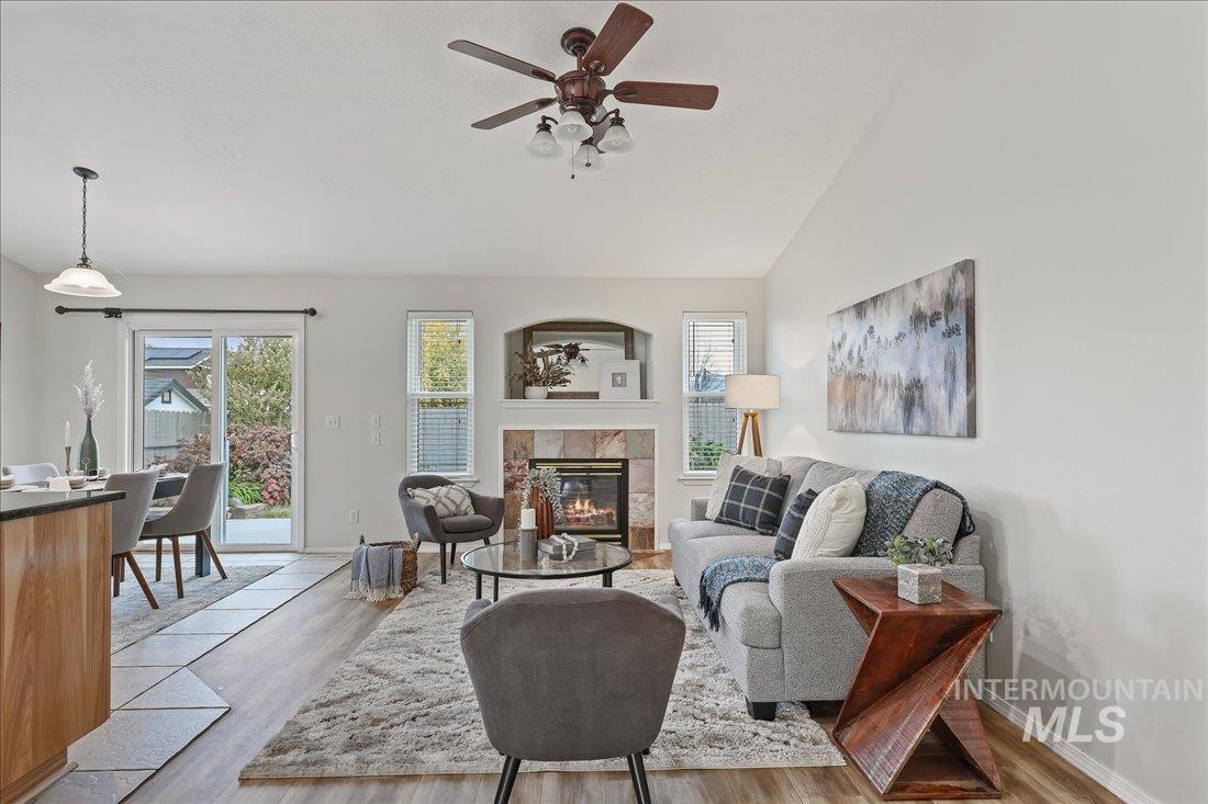 Living area with a tile fireplace, light wood-style floors, lofted ceiling, and ceiling fan