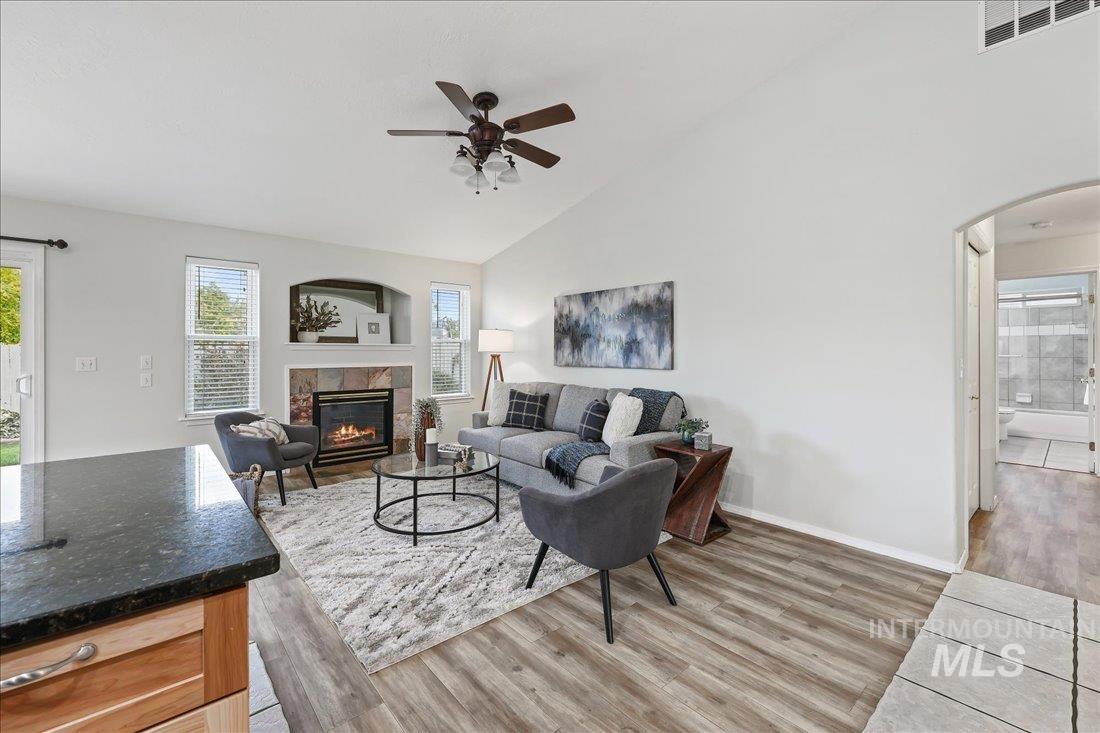 Living area with light wood-type flooring, arched walkways, a fireplace, high vaulted ceiling, and a ceiling fan