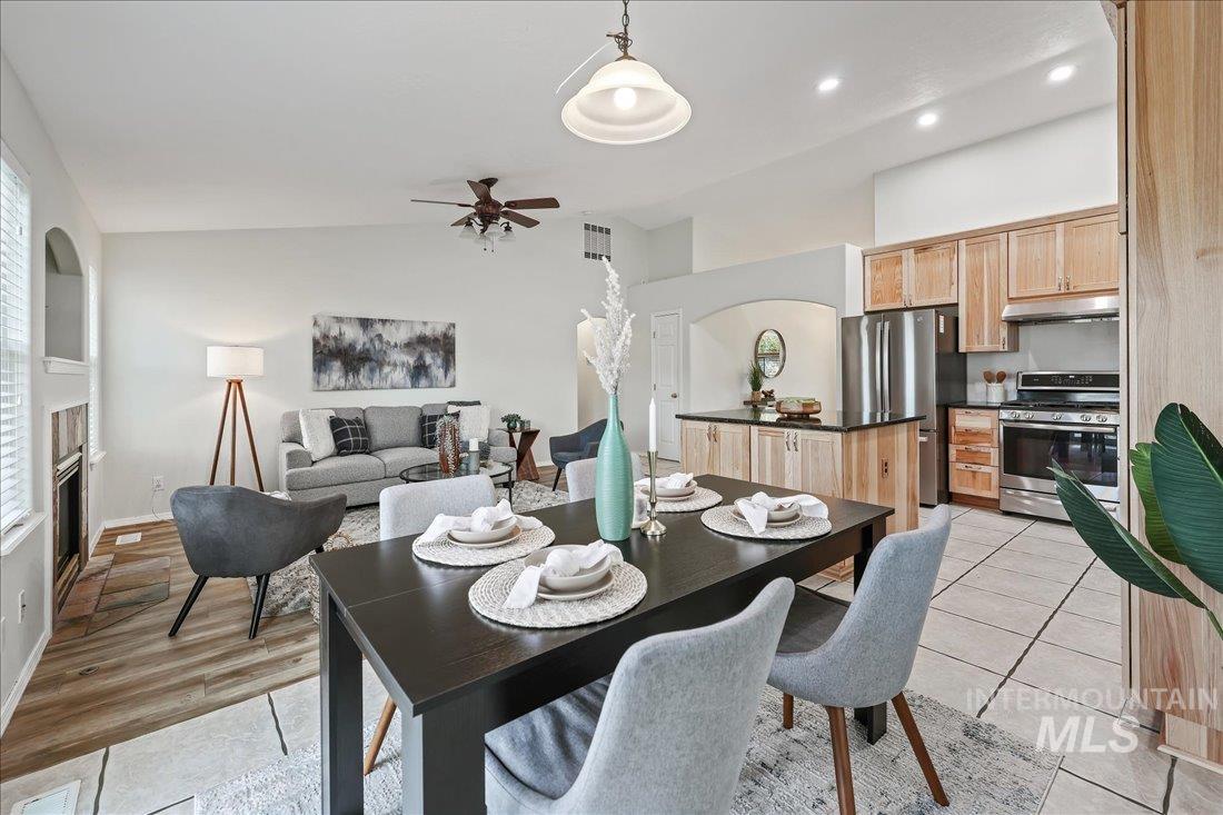Dining space with vaulted ceiling, ceiling fan, a glass covered fireplace, light tile patterned floors, and recessed lighting