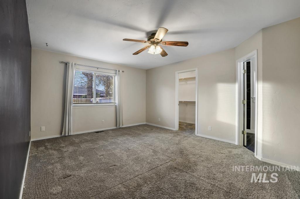 Unfurnished bedroom with a walk in closet, carpet floors, and a ceiling fan