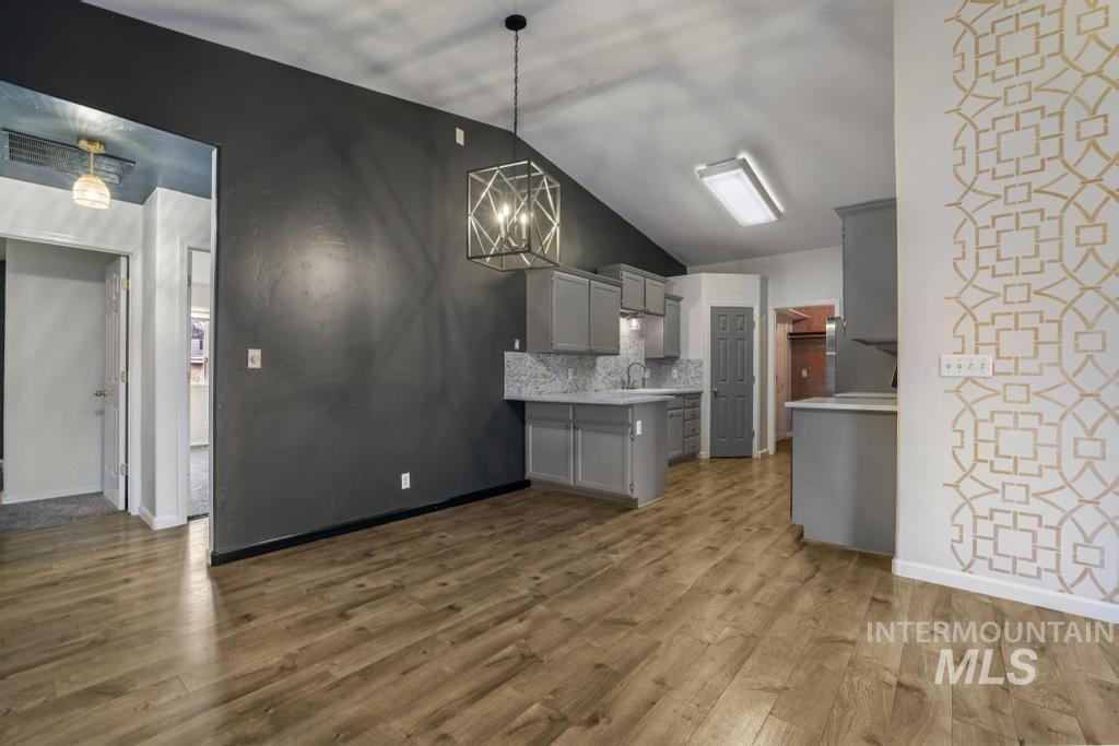 Kitchen with gray cabinetry, light countertops, vaulted ceiling, a chandelier, and dark wood-style floors