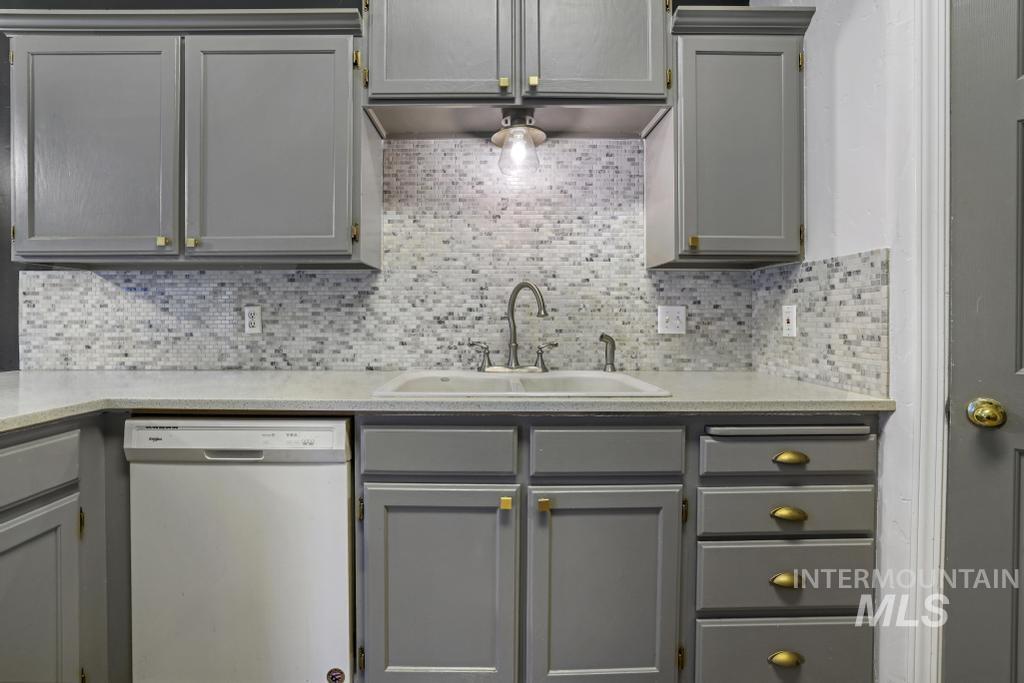Kitchen featuring gray cabinetry, dishwasher, decorative backsplash, and light stone countertops