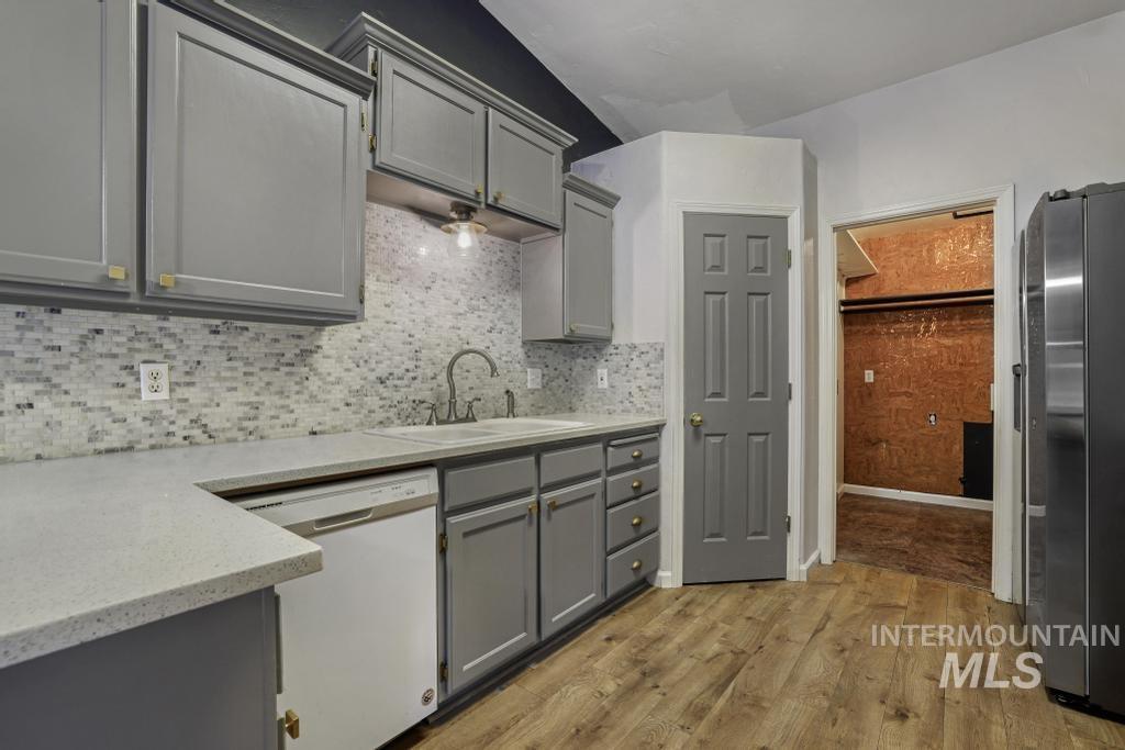 Kitchen with gray cabinetry, light wood-style flooring, white dishwasher, freestanding refrigerator, and backsplash
