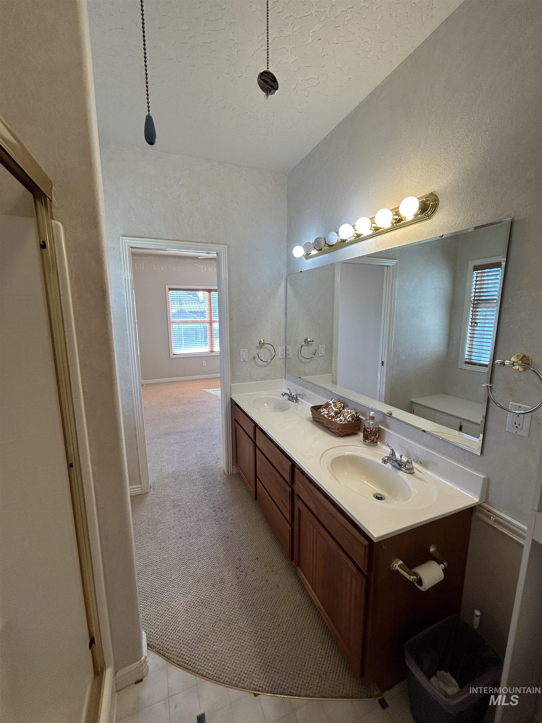 Bathroom featuring double vanity, a textured ceiling, light colored carpet, and a shower stall