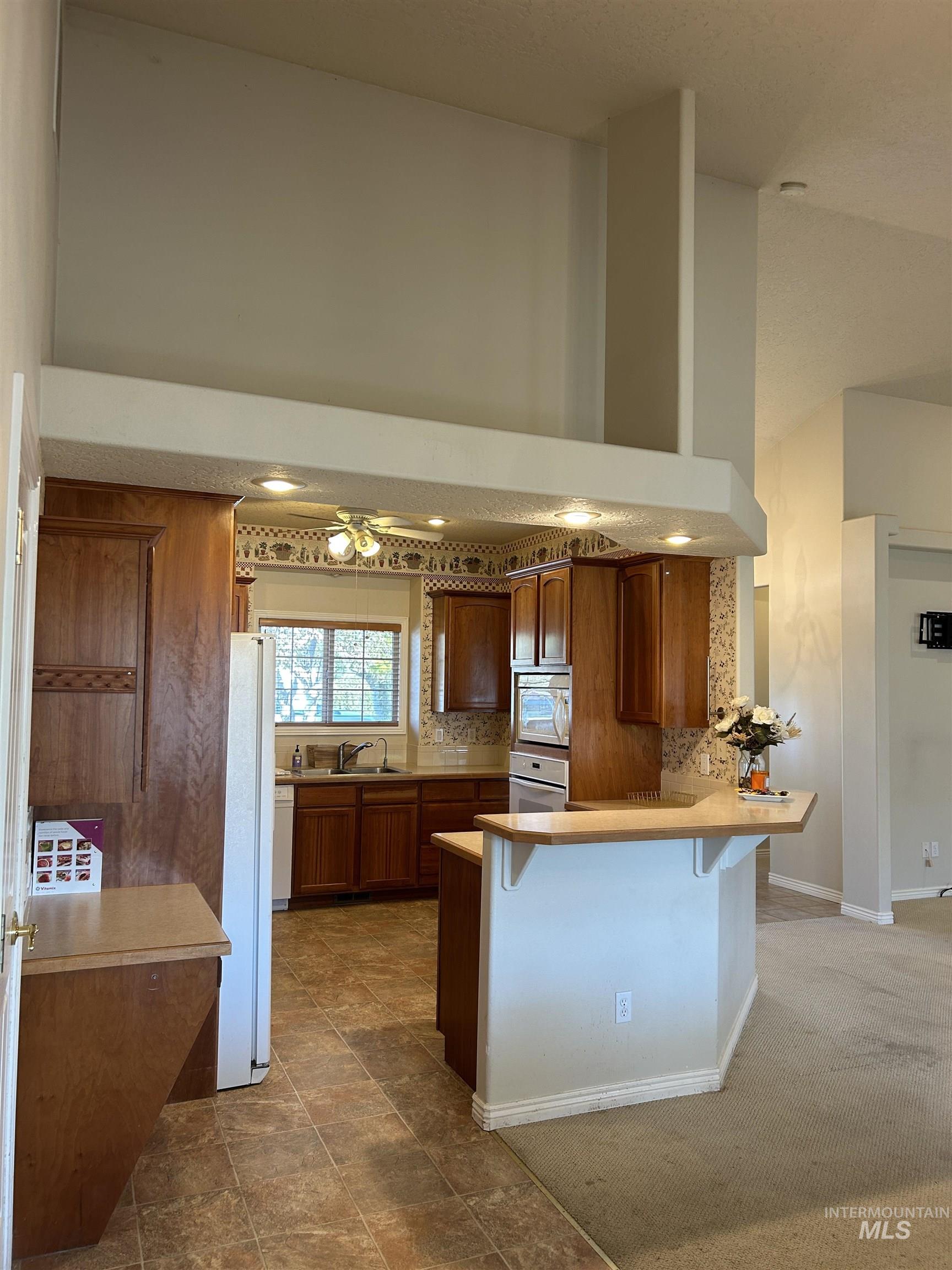 Kitchen with brown cabinetry, a kitchen breakfast bar, light countertops, decorative backsplash, and a peninsula