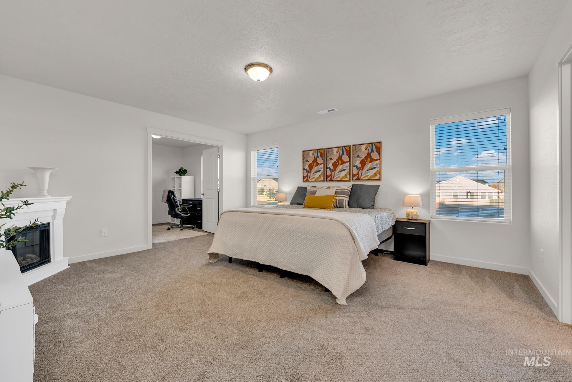 Bedroom with light carpet, a desk, a glass covered fireplace, and a textured ceiling