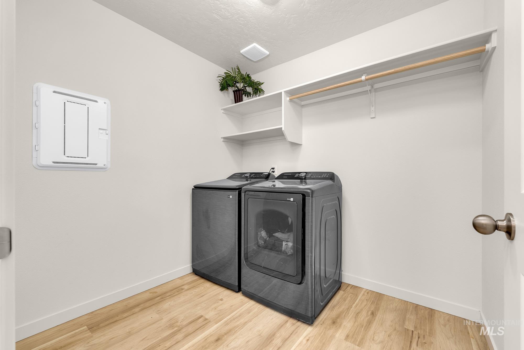 Laundry area with light wood-type flooring, washing machine and dryer, and a textured ceiling