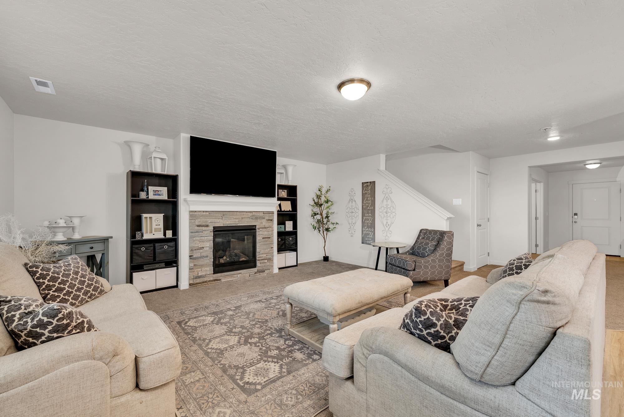Living room featuring a stone fireplace, a textured ceiling, and carpet