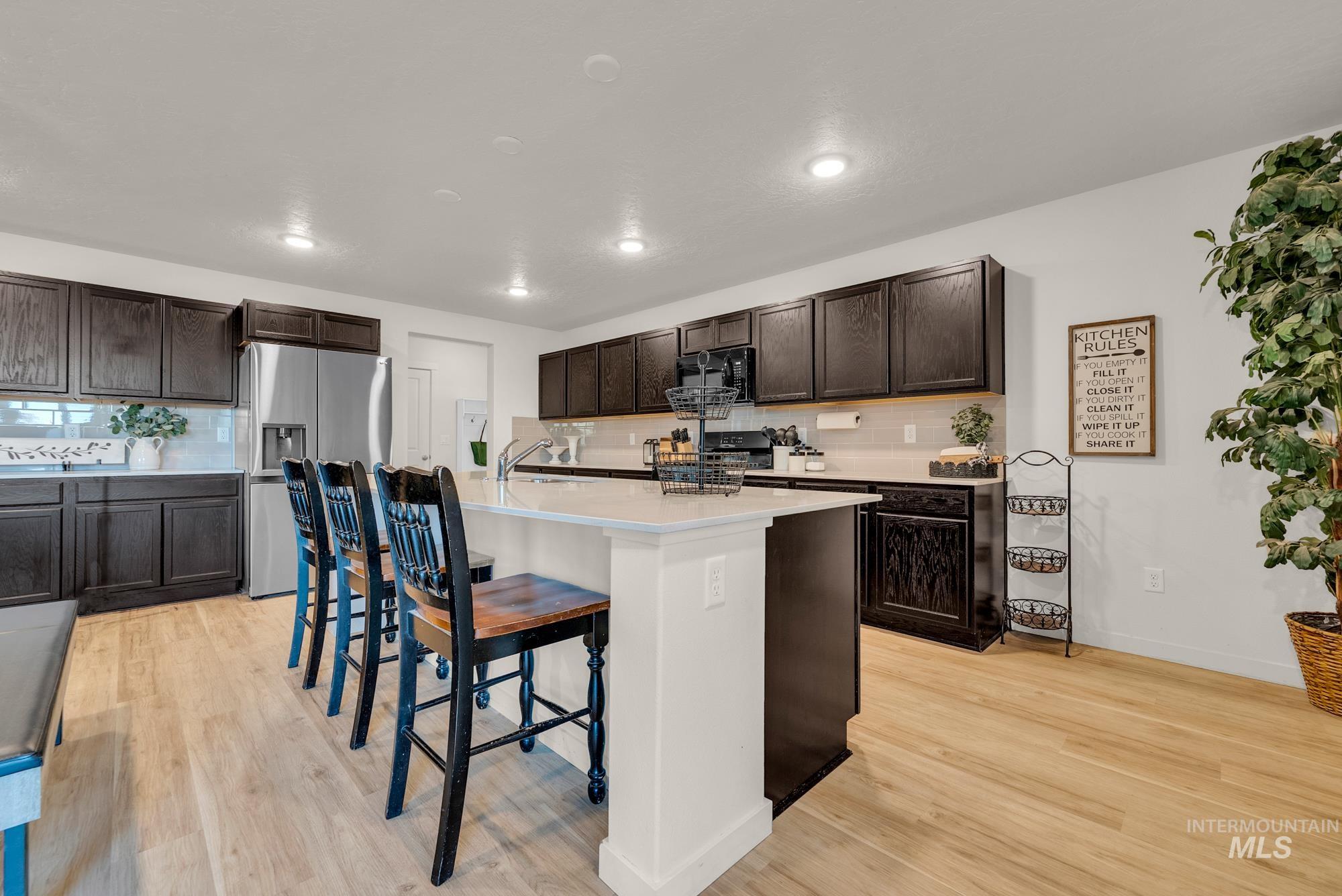 Kitchen featuring decorative backsplash, dark brown cabinetry, a kitchen bar, black appliances, and recessed lighting