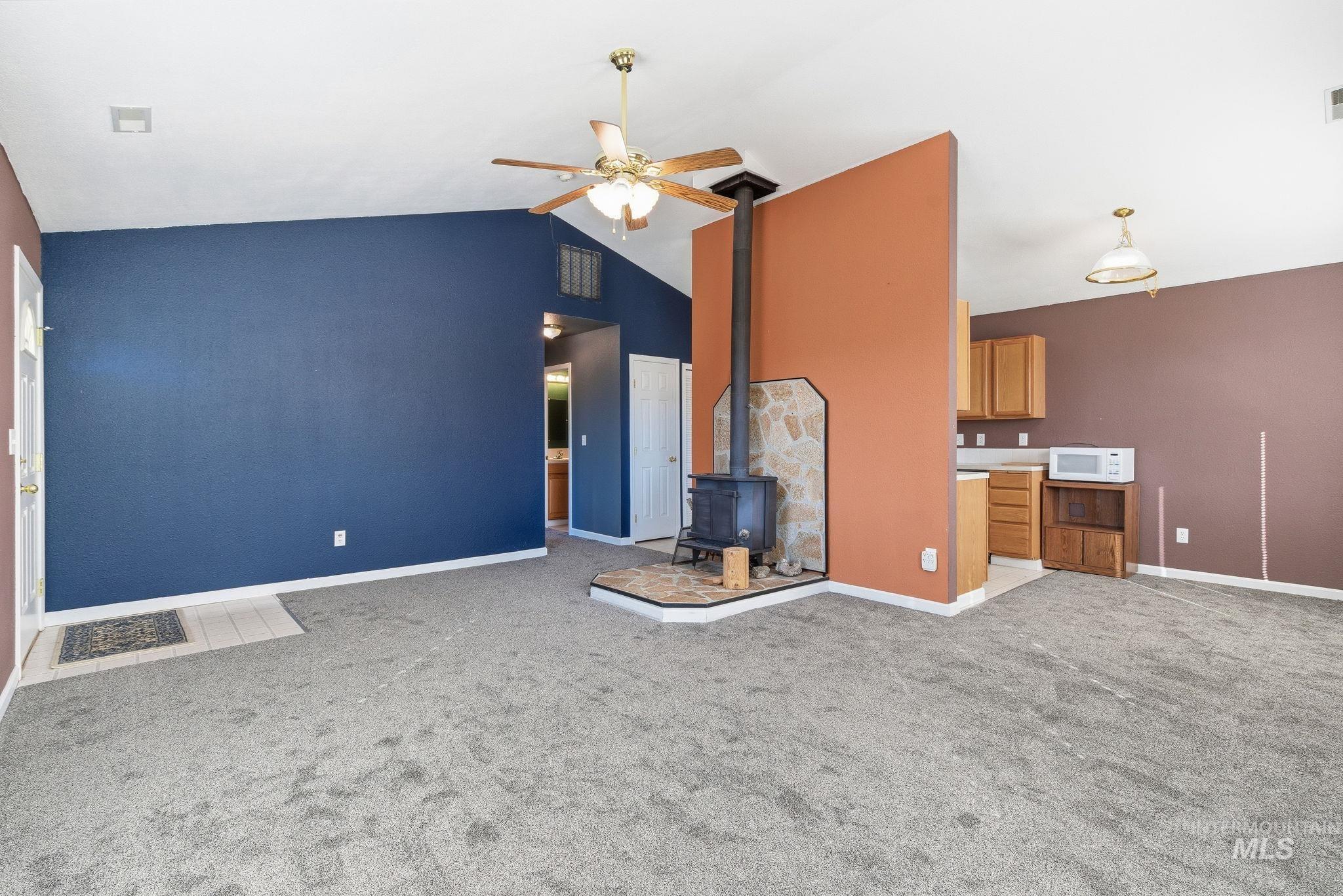 Unfurnished living room with a wood stove, light carpet, ceiling fan, and high vaulted ceiling