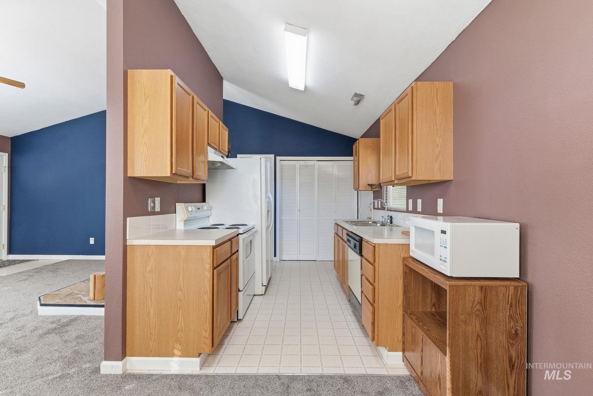 Kitchen featuring white appliances, light countertops, vaulted ceiling, light carpet, and light tile patterned floors