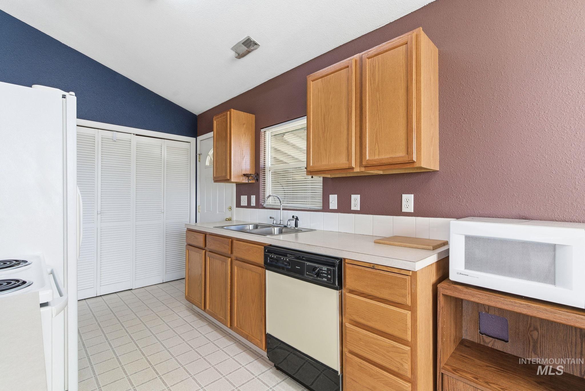 Kitchen with white appliances, light countertops, light tile patterned floors, vaulted ceiling, and a textured wall