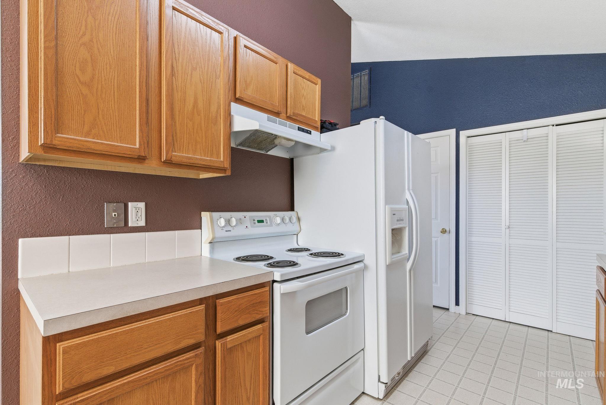 Kitchen featuring white appliances, under cabinet range hood, a textured wall, light tile patterned flooring, and light countertops