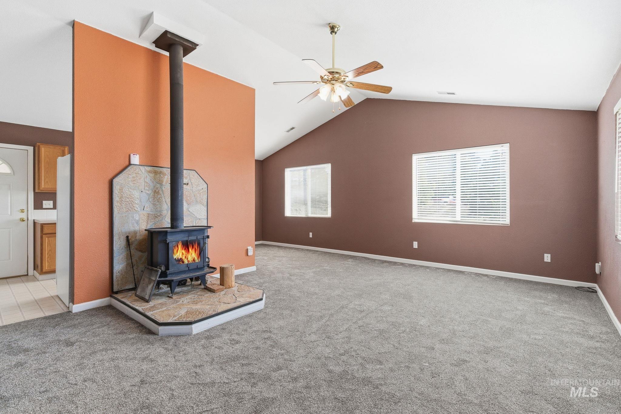 Unfurnished living room with a wood stove, lofted ceiling, light colored carpet, and a ceiling fan