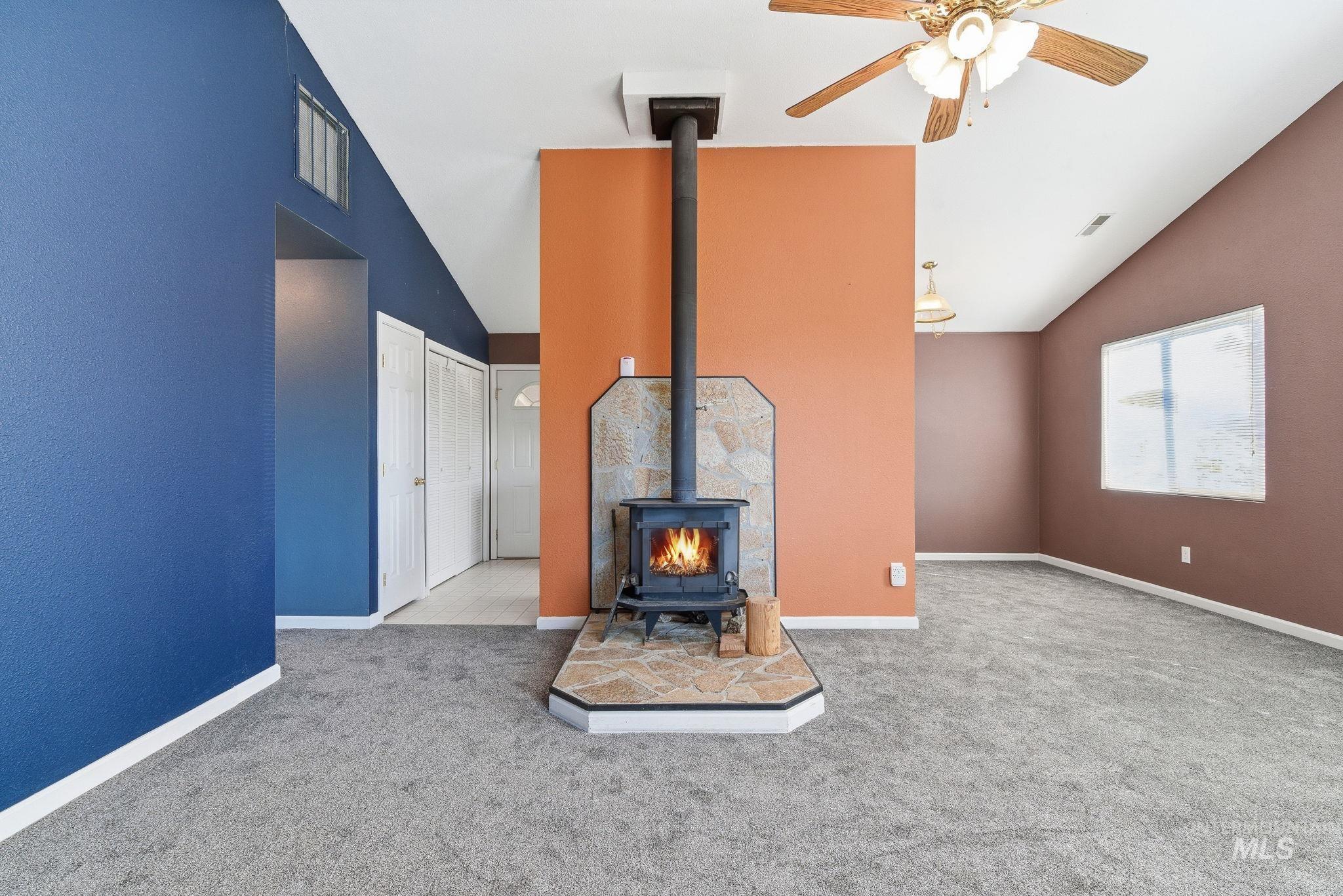 Unfurnished living room with a wood stove, carpet flooring, ceiling fan, and high vaulted ceiling
