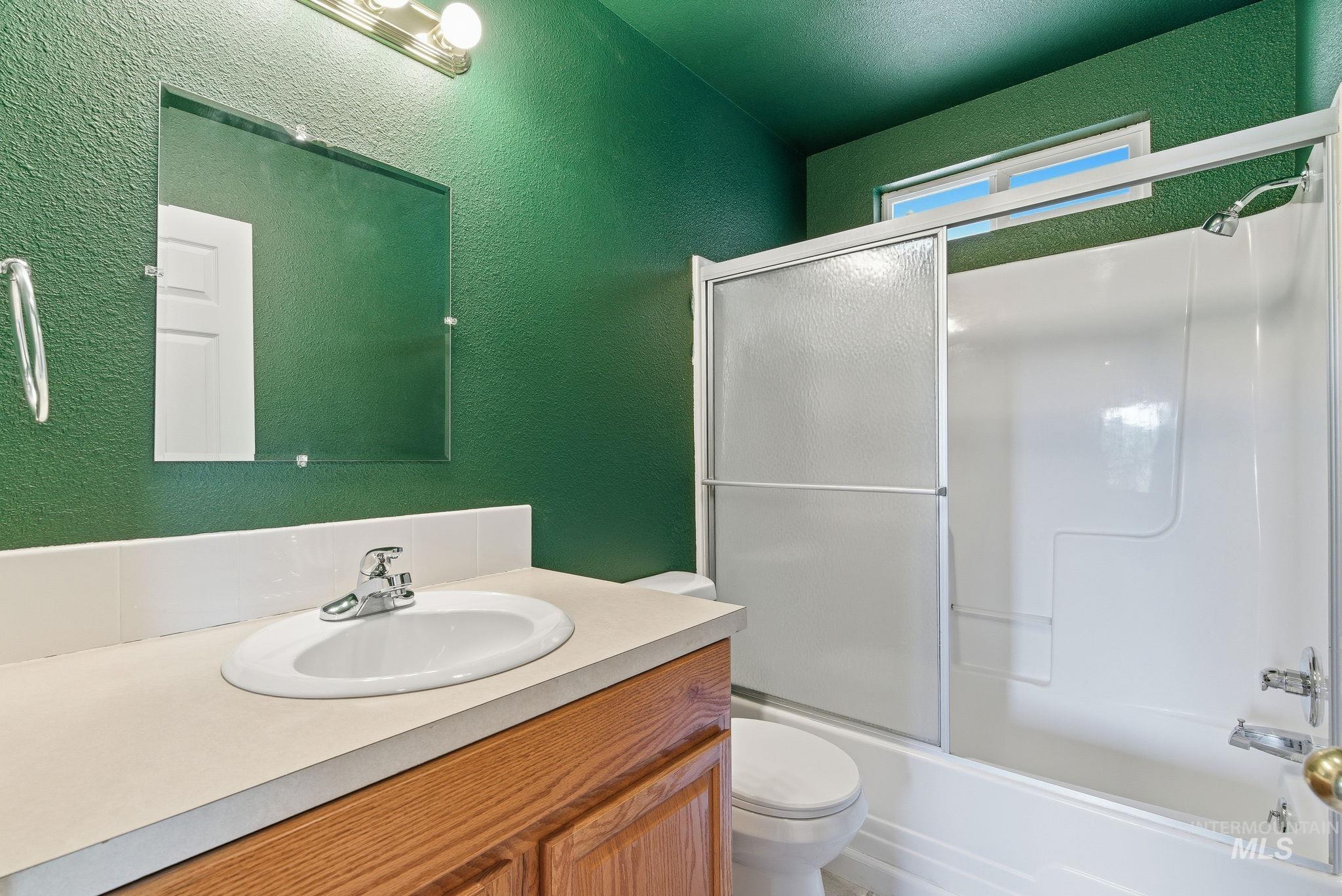 Bathroom with a textured wall, vanity, and bath / shower combo with glass door