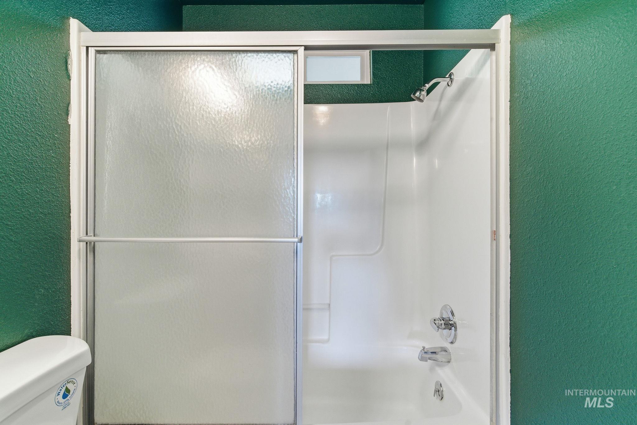 Bathroom with a textured wall and bath / shower combo with glass door