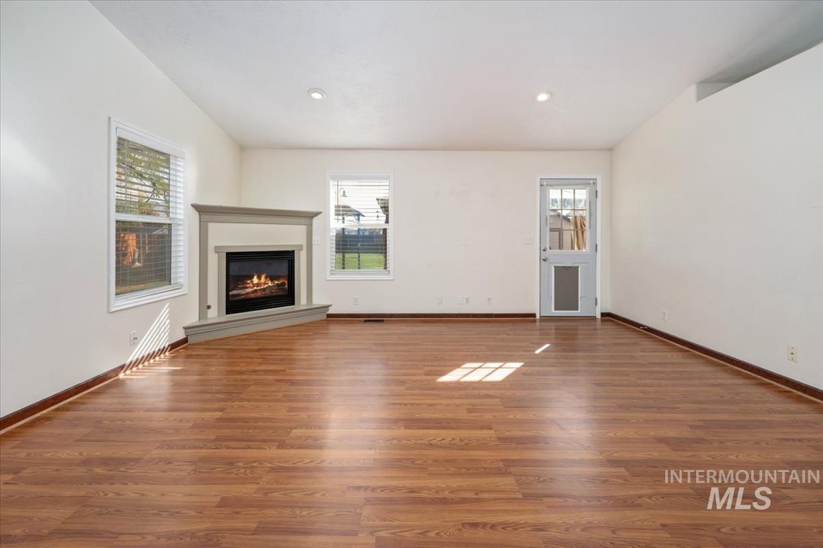 Unfurnished living room featuring a glass covered fireplace, wood finished floors, and recessed lighting