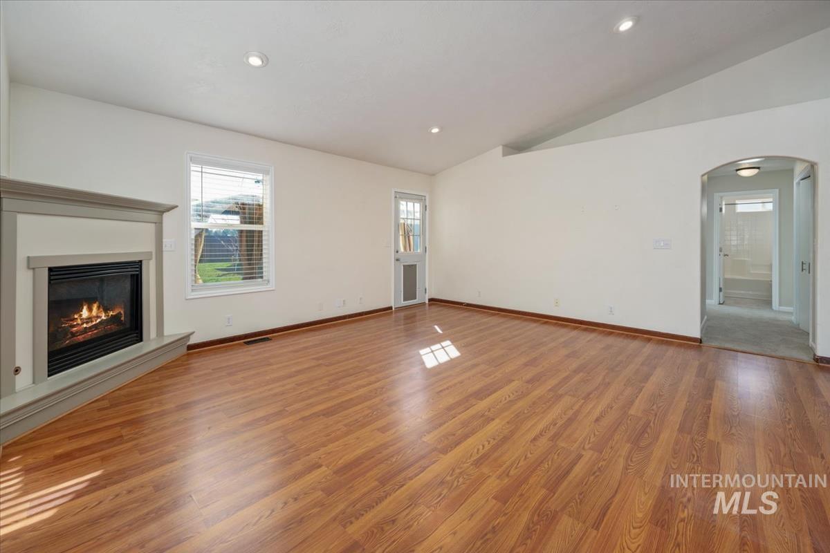 Unfurnished living room featuring recessed lighting, a glass covered fireplace, light wood-type flooring, vaulted ceiling, and arched walkways