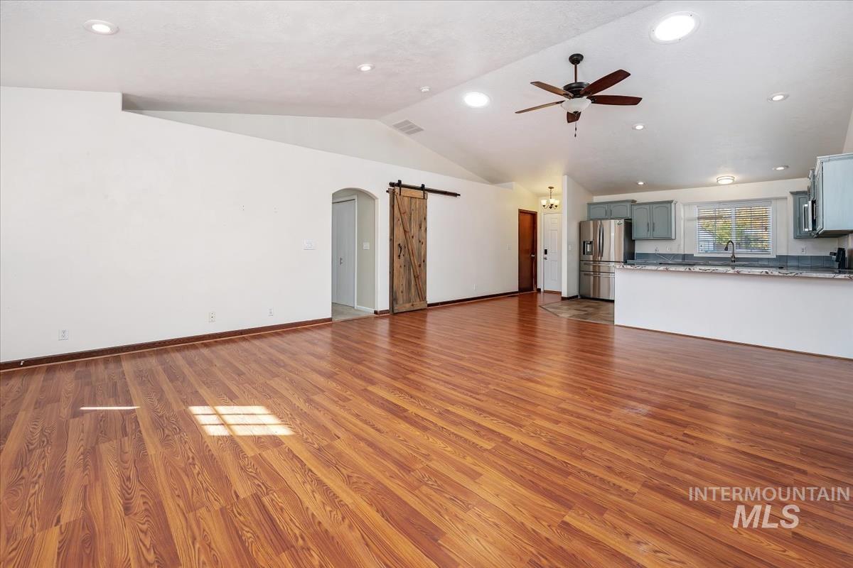 Unfurnished living room featuring a barn door, arched walkways, dark wood-style floors, lofted ceiling, and recessed lighting